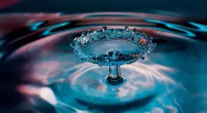 Close-up of a water droplet creating a crown-shaped splash on a blue rippling surface.