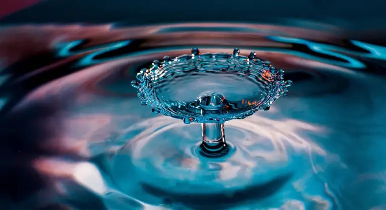 Close-up of a water droplet creating a crown-shaped splash on a blue rippling surface.