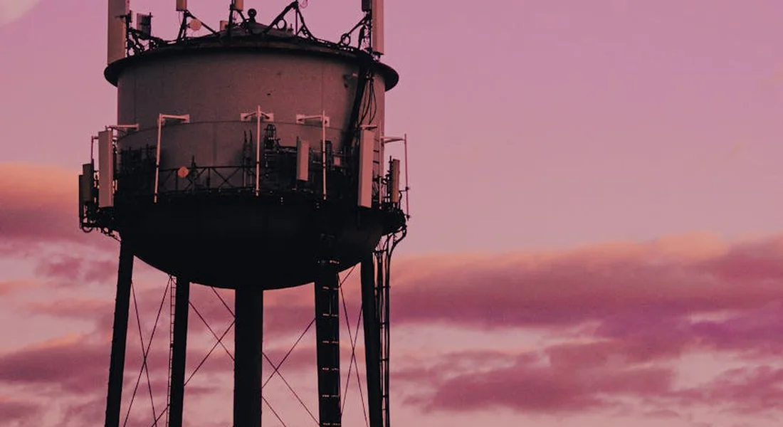 Elevated water storage tank on stilts silhouetted against a pink sunset.