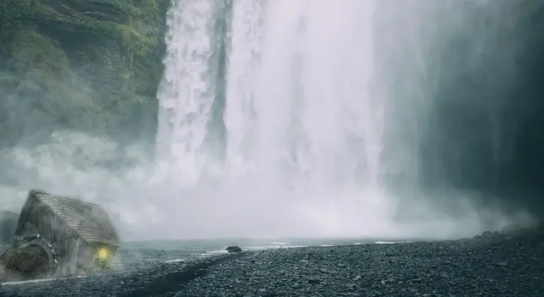 Wide scene of a powerful waterfall with mist, rocky foreground, and a dark, indistinct vehicle-like object on the left.
