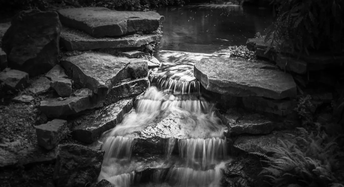 Black-and-white image of a cascading waterfall flowing over layered rocks