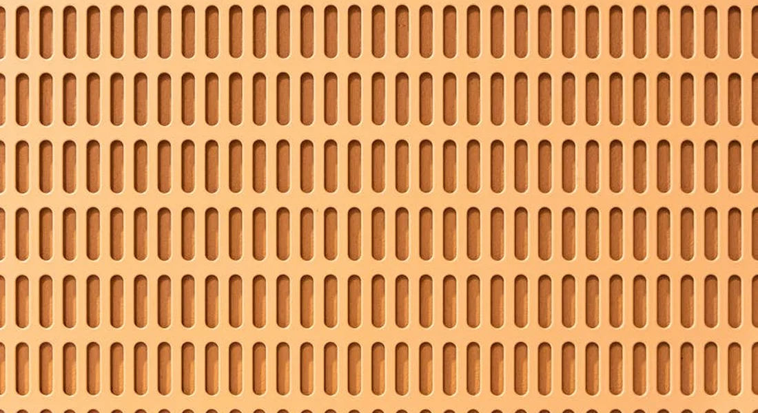 Close-up of a perforated orange vent surface with evenly spaced vertical slots.