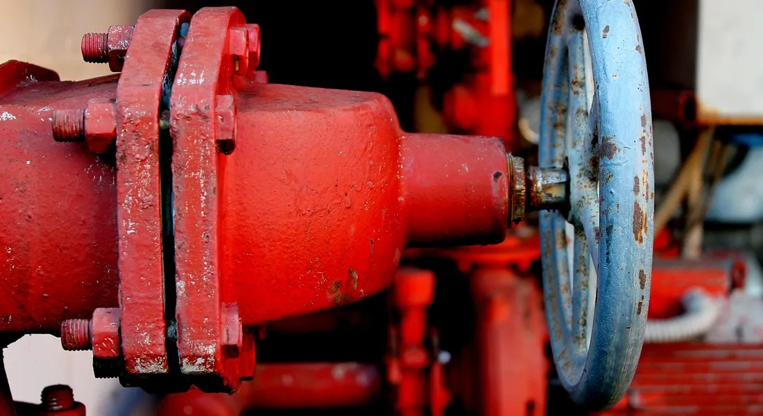 Close-up of a red industrial well pump with a blue handwheel, showing flanged connections and piping.