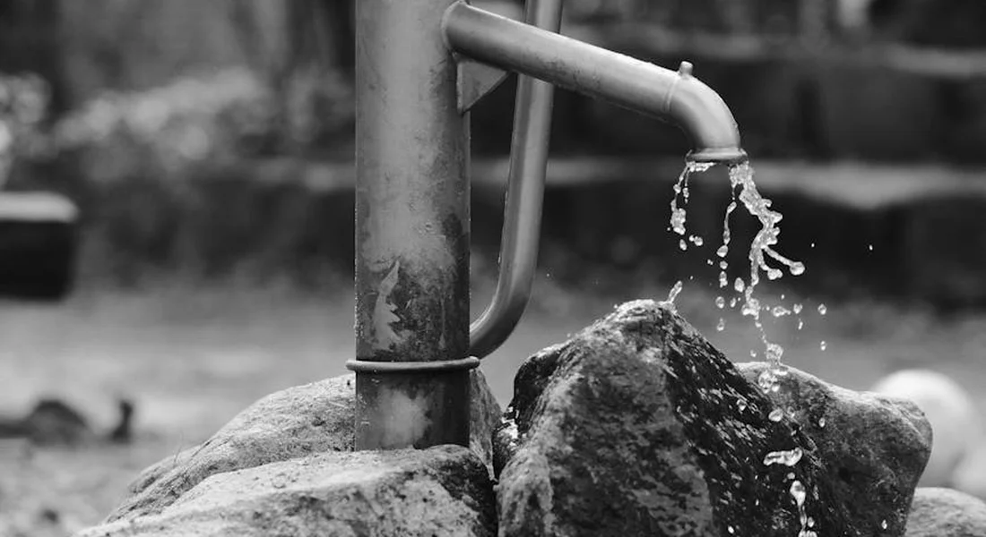 Close-up of a metal water spout dripping water onto rocks, illustrating plumbing work for a home pump replacement.
