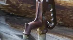 Close-up of a rusty hand-pump valve mounted on wood, representing well pump maintenance.