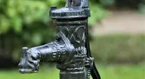 Close-up image of a metal well pump valve with a spigot, outdoors with a blurred green background.