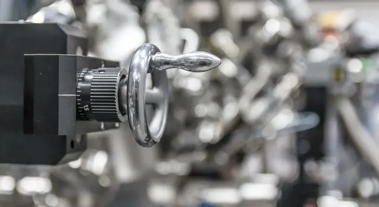Close-up of a metal well pump valve with a circular handwheel and knob, set against a blurred mechanical background.
