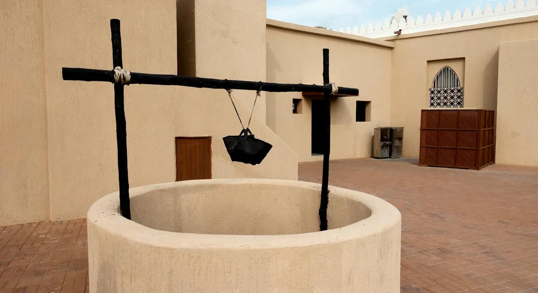 Outdoor masonry well with a black metal frame and a hanging bucket in a courtyard