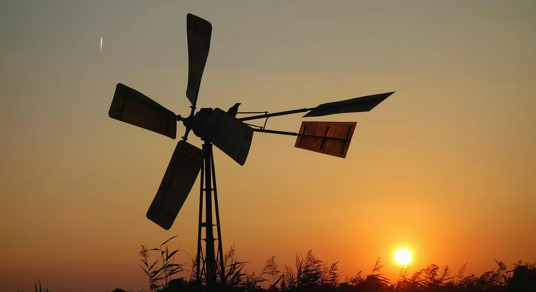 Silhouette of a windmill against an orange sunset with tall grasses