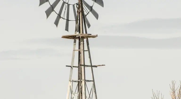 An old windmill standing in a rural field against a pale sky.