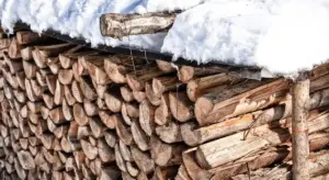 Stack of split firewood under snow with a wooden beam on top