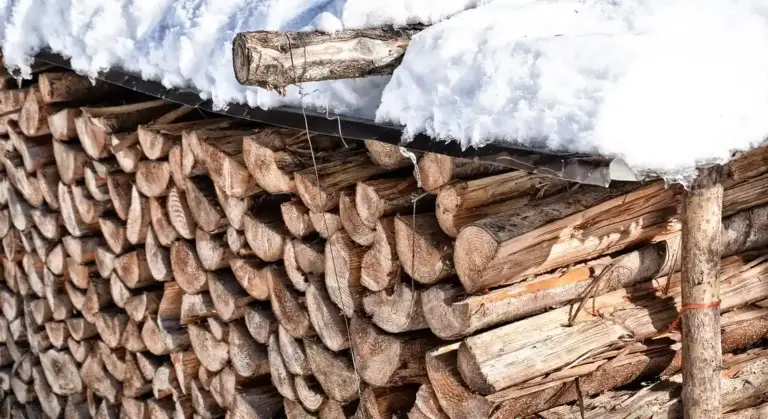 Stack of split firewood under snow with a wooden beam on top