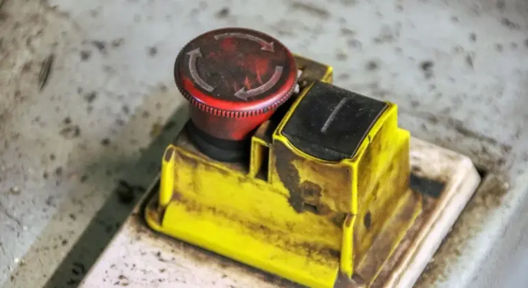 Close-up of a yellow sump pump float switch with a red adjustment knob, showing dirt and grime on the housing.