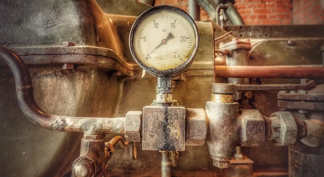 Close-up image of a pressure gauge attached to a rusty water pressure tank with metal pipes and fittings