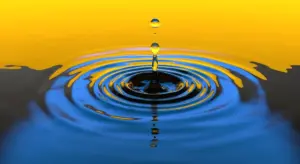Close-up of a water droplet creating ripples on a blue and yellow water surface.